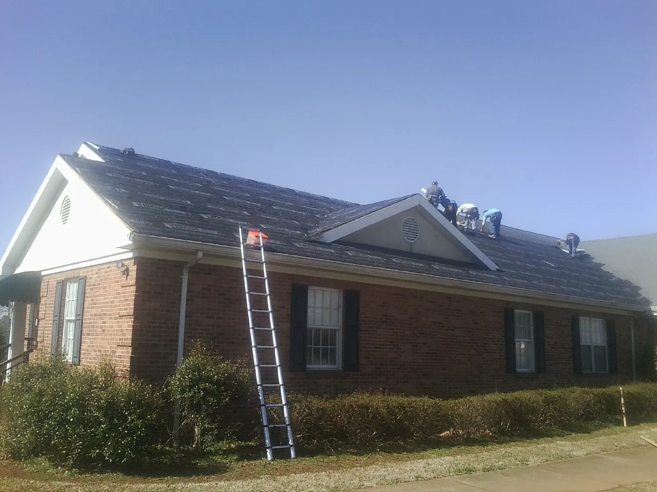 Crew tearing shingles off a brick ranch roof with a ladder set — Emergency Roof Repair work by our crew in Haubstadt