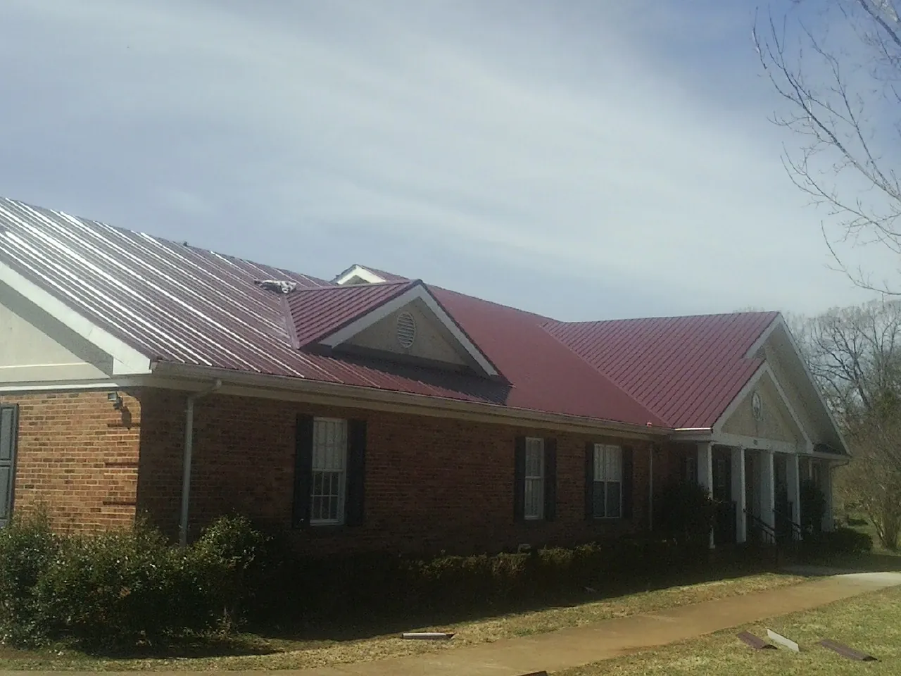 Red metal roof with gabled entries on a long brick building, from a Hail Damage Roof Repair job in Haubstadt