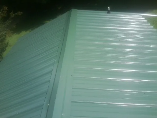 New green metal panels meeting at the ridge of a roof — Flat Roof Repair work by our crew in Haubstadt