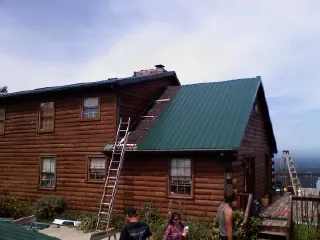 Green metal roof going on a two story log home with ladders set in Haubstadt