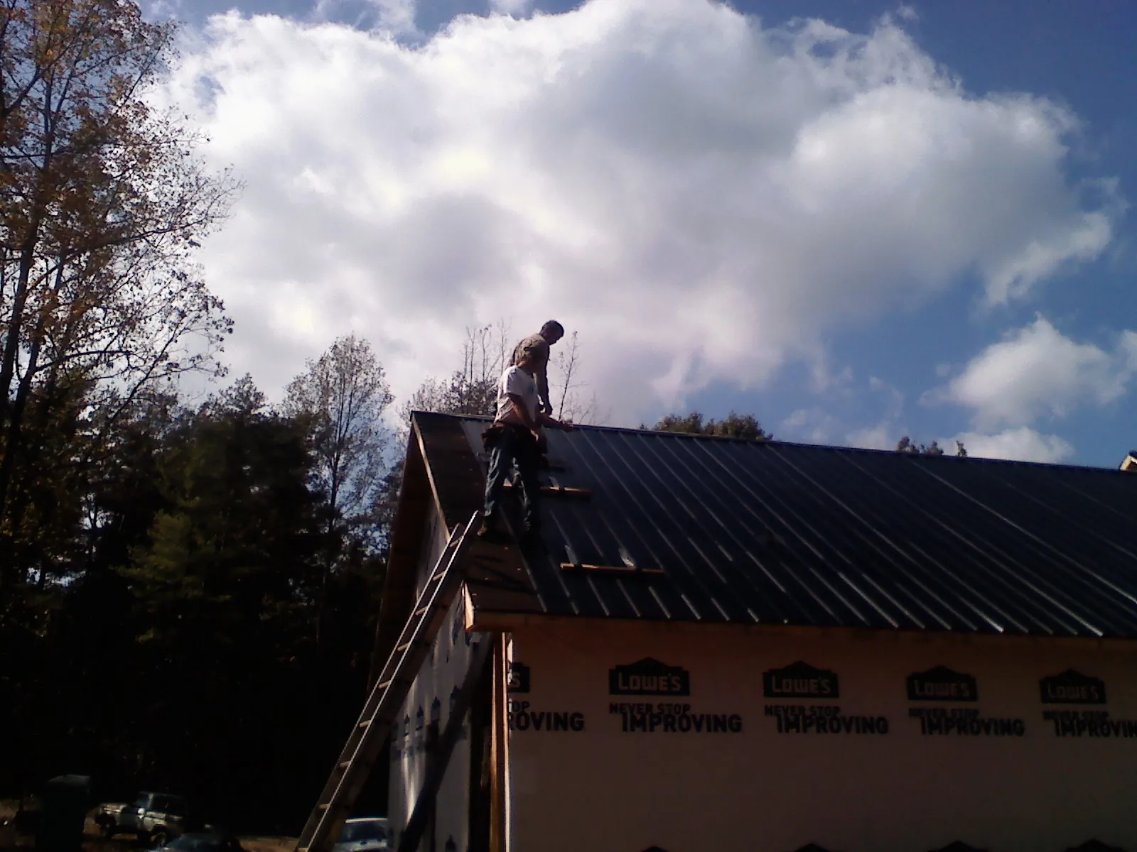 Roofer fastening dark metal panels high against a cloudy sky, from a Roof Inspection job in Haubstadt