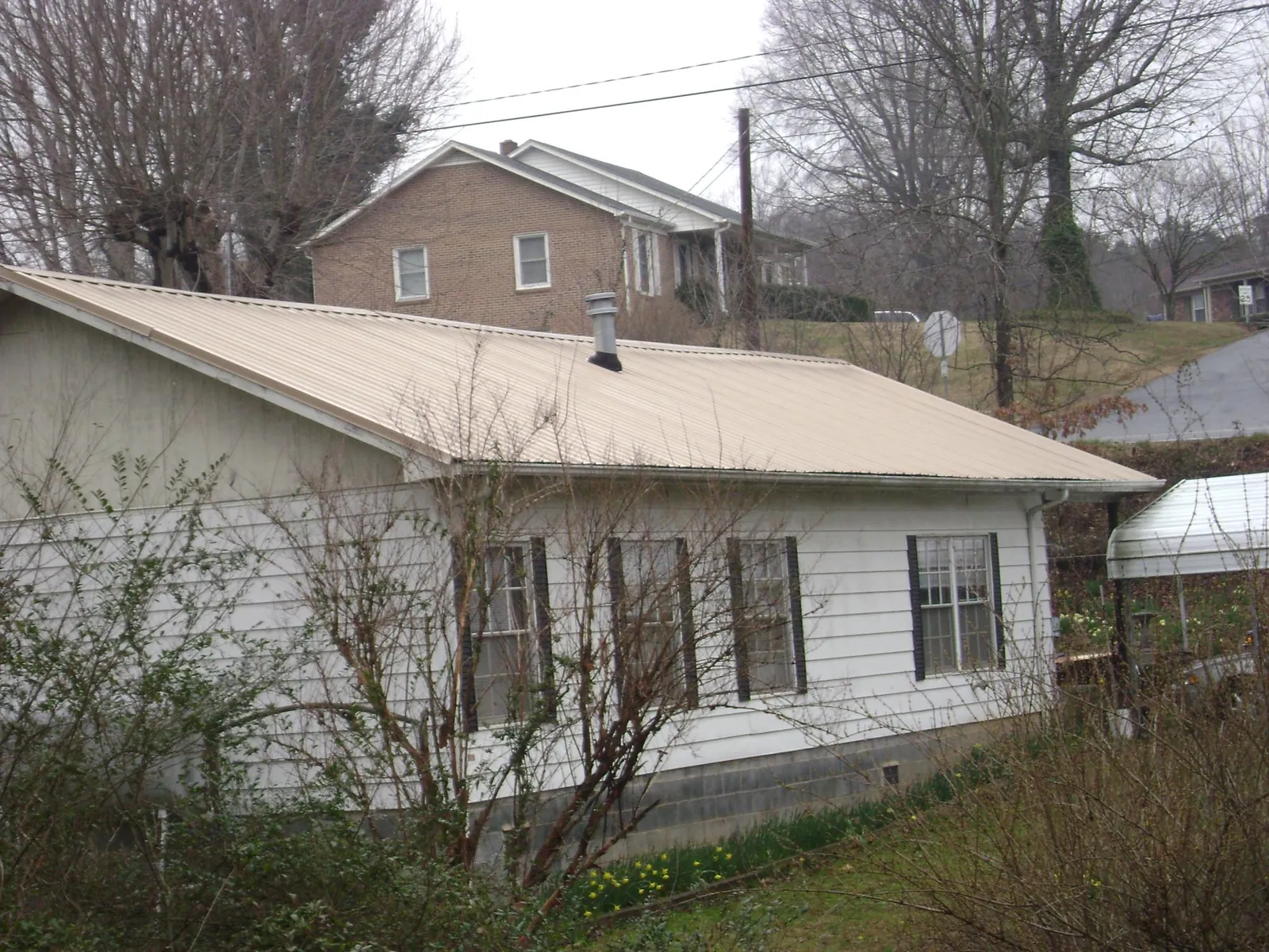 Tan metal roof on a white sided house set into a hillside — Commercial Roofing by Roofing Brothers in Haubstadt